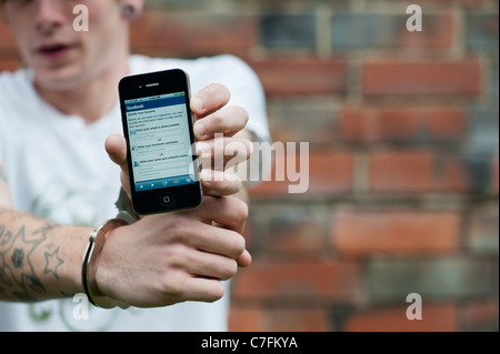 Gefesselte Teenager halten Sie ein Apple Iphone zeigt Facebook. Stockfoto