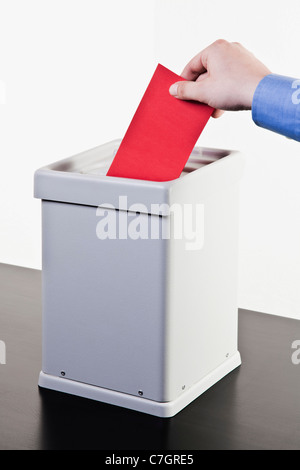 Ein Mann, einen leeren roten Stimmzettel in eine Wahlurne, close-up Hände Stockfoto