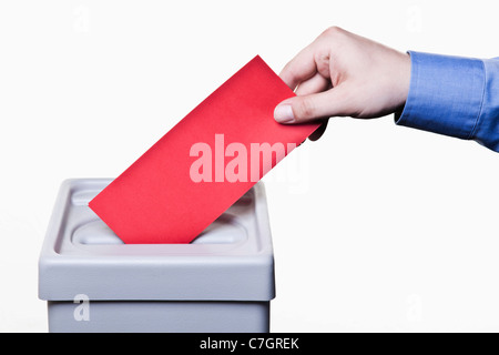 Ein Mann, einen leeren roten Stimmzettel in eine Wahlurne, close-up Hände Stockfoto