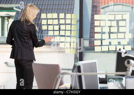 Geschäftsfrau, kleben viele Notizen zu ihrem Bürofenster Stockfoto
