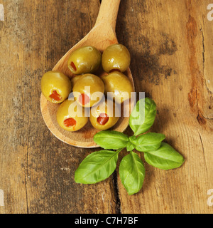 Oliven mit einem Zweig Basilikum in einem Holzlöffel auf einem Hintergrund von alten geknackt und verwitterte Holz Stockfoto