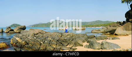 Panoramablick auf eine Frau tun Meditation Yoga auf den Felsen an einem Strand in einem tropischen Ambiente Stockfoto