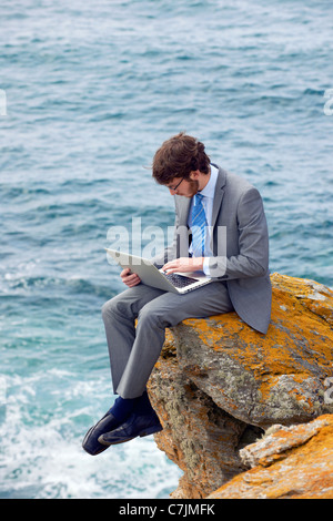 Geschäftsmann mit Laptop auf Klippe Stockfoto
