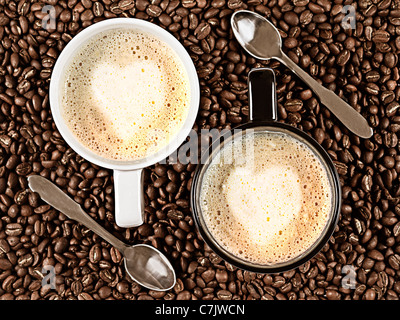 Zwei Tassen mit Cafee Latte mit Herz geformt Rosetta umgeben von Kaffeebohnen und Löffel Stockfoto