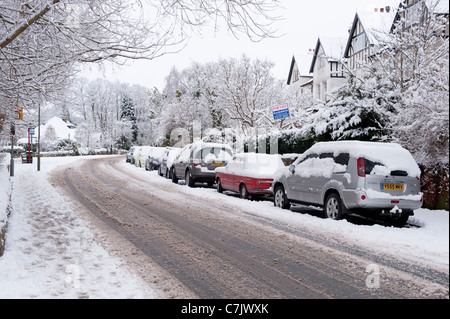 Winter Village Street (Autospuren auf ruhiger schneebedeckter Straße, Autos geparkt, Fußspuren auf menschenleerem Bürgersteig) - Burley in Wharfedale, England, GB, UK. Stockfoto