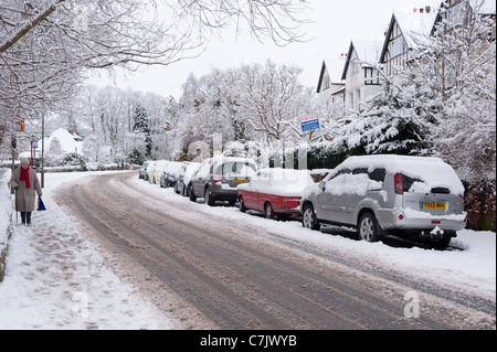 Winter Village Street (Spuren auf schneebedeckten Straße, Autos geparkt, Fußgänger zu Fuß, Fußabdrücke auf Bürgersteig) - Burley in Wharfedale, England, GB, Großbritannien. Stockfoto