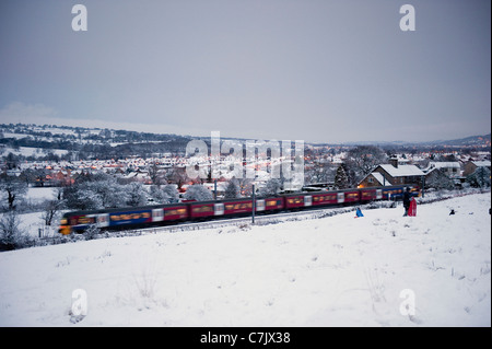 Schneebedeckter Winterabend, Personenzug, der an ländlichen Dörfern vorbeifährt und weißes schneebedecktes Feld - Wharfedale Line, West Yorkshire, England, Großbritannien. Stockfoto