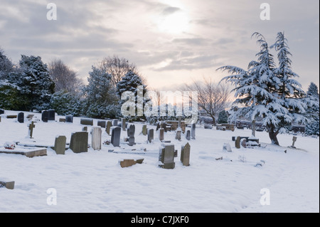 Schneebedeckter Sonnenuntergang am Winterabend - Gräber und Kopfsteine auf ruhigem, weißem, schneebedecktem ländlichem Friedhof oder Friedhof - Guiseley, West Yorkshire, England, Großbritannien. Stockfoto