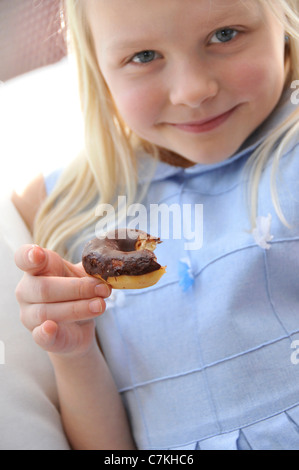 Junges Mädchen, 6, mit einem blauen Kleid und ein Schoko Donut in ihrer hand Stockfoto