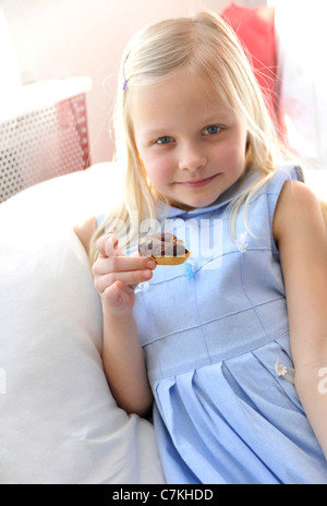 Junges Mädchen, 6, mit einem blauen Kleid und ein Schoko Donut in ihrer hand Stockfoto