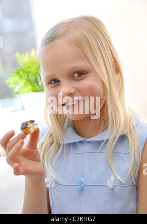 Junges Mädchen, 6, mit einem blauen Kleid und ein Schoko Donut in ihrer hand Stockfoto