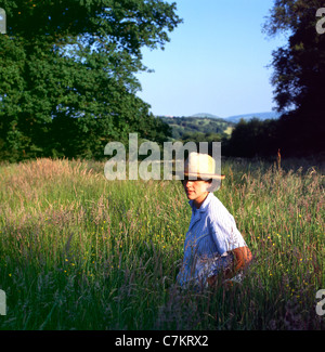 Eine junge Bäuerin der 1980er Jahre trägt einen Strohhut sitzend In einer im Heufeld blühenden Graswiese im Sommer in Die walisische Landschaft Carmarthenshire Wales Großbritannien KATHY DEWITT Stockfoto