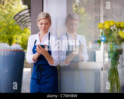 Porträt von schönen kaukasische Mädchen selbstständiger im Blumenladen, lächelnd und Mobiltelefon zu benutzen. Horizontale Form, Hüfte aufwärts Stockfoto