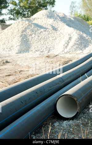 Schwarze Rohre und haufenweise Sand im Hintergrund. Vertikales Bild Stockfoto