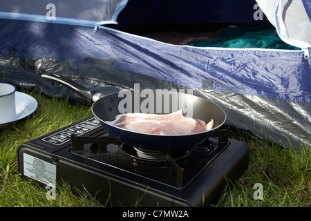 Braten Speck auf einen kleinen tragbaren Gaskocher vor einem offenen Zelttür Stockfoto