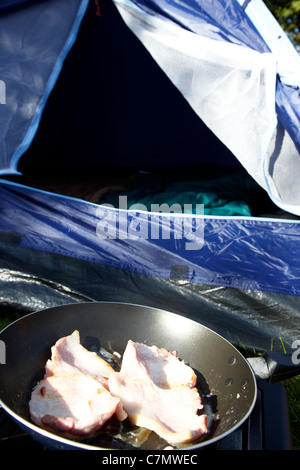 Braten Speck auf einen kleinen tragbaren Gaskocher vor einem offenen Zelttür Stockfoto