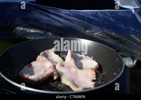 Braten Speck auf einen kleinen tragbaren Gaskocher vor einem offenen Zelttür Stockfoto