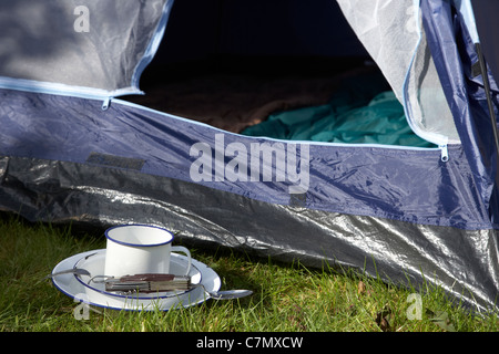 Weissblech Cup und camping-Werkzeug-Utensilien vor die offene Tür eines Zeltes Stockfoto