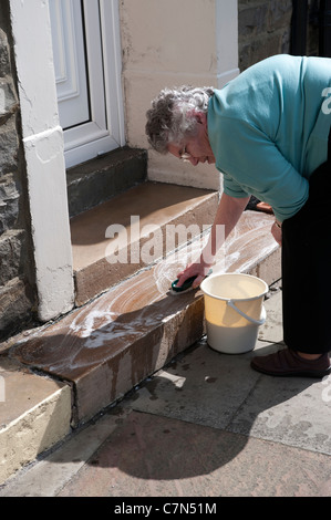 Schrubben ihre Haustür eine alte Dame in das Dorf der Middleton-in-Teesdale, Teesdale, County Durham, England, UK. Stockfoto