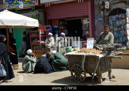 Ägypten.  Riverside Stadt Esna am Markttag.   Mann, Verkauf von Kartoffeln auf seinem Karren Männer hocken und diskutieren im Hintergrund. Stockfoto