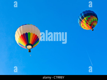 Zwei Heißluftballons auf ein blauer Himmel mit weißen Schweif von einem Flugzeug in die Ferne treiben Stockfoto