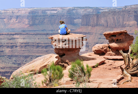 Junge Frau sitzt auf einem flachen Felsen im Dead Horse Point State Park, in der Nähe von Moab, Utah Stockfoto