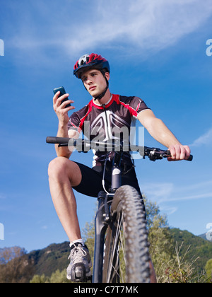 sportlichen Aktivität: junge Erwachsene Radsportler, Mountainbike und SMS auf Handy. Vertikale Form, niedrigen Winkel Ansicht Stockfoto