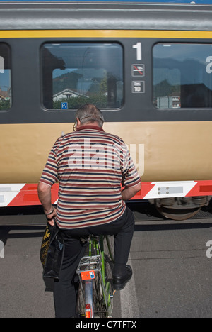 Radfahrer an einem Bahnübergang wartet, während die Barriere für das Bestehen eines Zuges ist Stockfoto