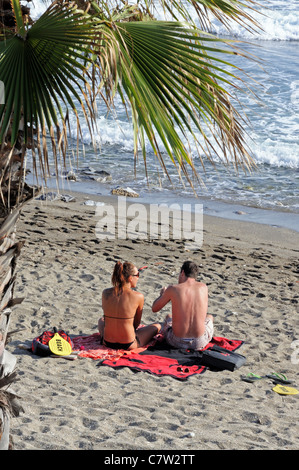 Paar am Strand, Marbella, Costa del Sol, Provinz Malaga, Andalusien, Spanien, Westeuropa sitzt. Stockfoto