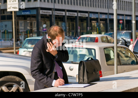 Geschäftsmann am mobilen im freien sprechen und schreiben auf notebook Stockfoto