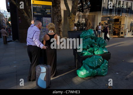 Elegant gekleidete paar prüfen eine Karte von London Straßen in der Nähe von Abfallsäcke in Long Acre im Herzen der Hauptstadt West end. Stockfoto