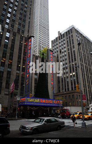 Business Frau Kreuzung Straße mit gelben Taxis und Mietwagen vor roten Neon Radio City Music Hall, 6th Avenue, New York City Stockfoto