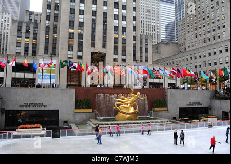 Ansicht-Eis - Skater, weiße Eisfront vergoldet Prometheus Skulptur GE Building Fahnen, Rockefeller Ice Rink, New York City Stockfoto