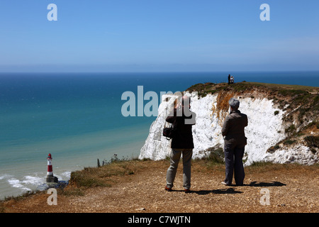 Touristen, die Blick auf Beachy Head, Leuchtturm im Hintergrund, in der Nähe von Eastbourne, East Sussex, England Stockfoto