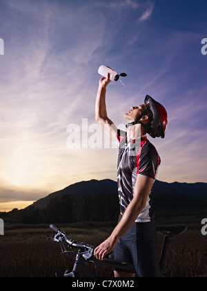 sportlichen Aktivität: jungen Erwachsenen Radfahrer auf Mountainbike Verschütten von Wasser auf Gesicht aus der Flasche. Vertikale Form, Seitenansicht, Textfreiraum Stockfoto