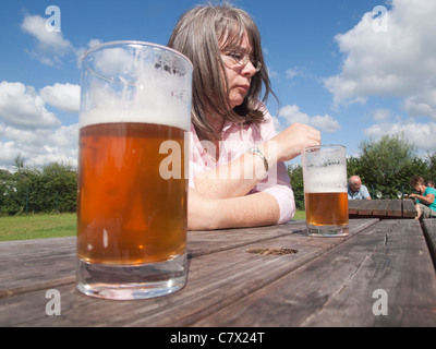 Nachdenkliche Frau in einem Biergarten an einem sonnigen Tag mit zwei halbvolle Gläser Bier auf der Ebene Holztisch Stockfoto