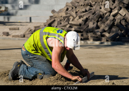 Ein Arbeiter verlegen neue Pflastersteine auf einer Baustelle in einem Zeitraum von heißem Wetter Stockfoto