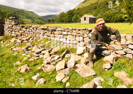 Eine Mann repariert eine Trockenmauer an Muker im Swaledale in North Yorkshire, England, Großbritannien, Uk Stockfoto