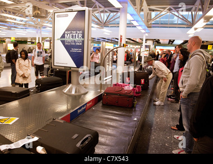 Die Fluggäste sammeln ihr Gepäck in der Gepäckhalle, terminal 3, Heathrow Flughafen London UK Stockfoto