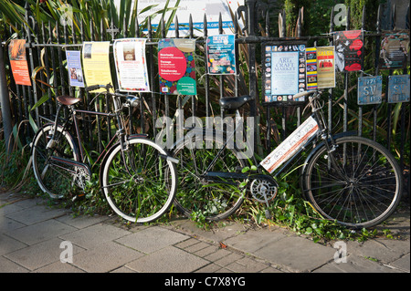 Zyklen, angekettet an Eisengitter in Cambridge Cambridgeshire England UK mit Plakaten an die Reling Werbeveranstaltungen befestigt. Stockfoto