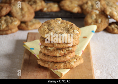 Ein Stapel von weißen Schokostückchen und Walnuss Cookies auf einem Holzbrett mit Cookies im Hintergrund Stockfoto