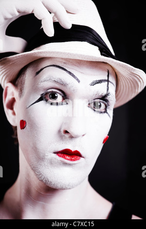 Studio-Porträt von Ernst theatralischen Clown in weißen Hut mit roten Herzen auf ihrem Gesicht auf schwarzem Hintergrund isoliert Stockfoto