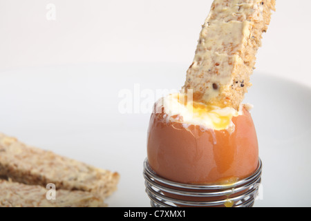 Ein leicht geröstetes Stück Getreidespeicher Brot tauchte in ein weich gekochtes Ei auf einem weißen Teller Stockfoto