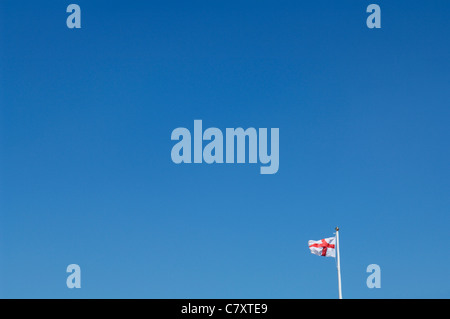 Eine entfernte St Georges Cross Flagge von England vor einem strahlend blauen Himmel. Stockfoto