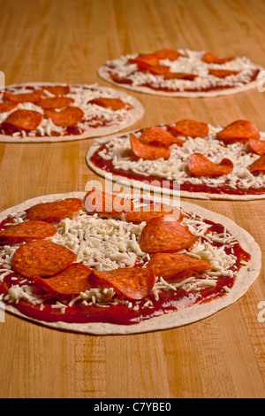 Vier ungekocht Salami und Käse Tortilla Pizza auf einer langen hölzernen Oberfläche Stockfoto