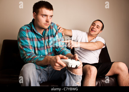 Junger Mann immer ausgelacht, als er zum anderen verliert, während eines Video-Spiels Stockfoto