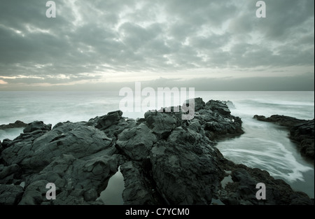 Flut als Bewegungsunschärfe an einem steinigen Strand während der Dämmerung Stockfoto