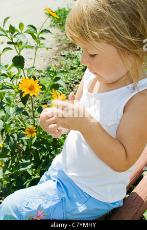 Kleines Mädchen hält Blume und sitzt auf der Bank im park Stockfoto