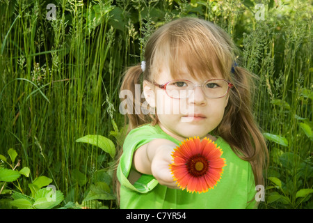 Kleines Mädchen sitzt in den Rasen und die rote Blume in der Hand hält Stockfoto