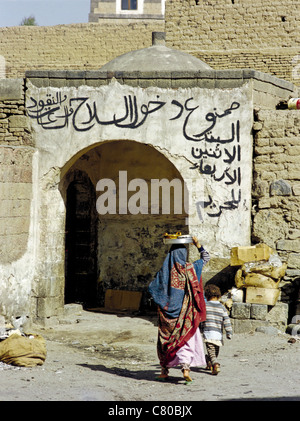 Jemenitische Frau und Kind betreten eines Gebäudes mit arabische Schrift über der Tür in der alten Stadt von Sana'a, Jemen Stockfoto